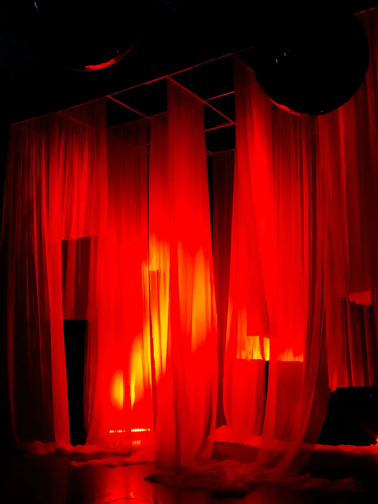 Telas iluminadas en rojo y naranja sobre un escenario, expresión y voz
