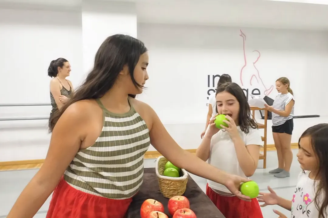 Alumnas de la escuela juegan una escena con una cesta de manzanas como atrezo